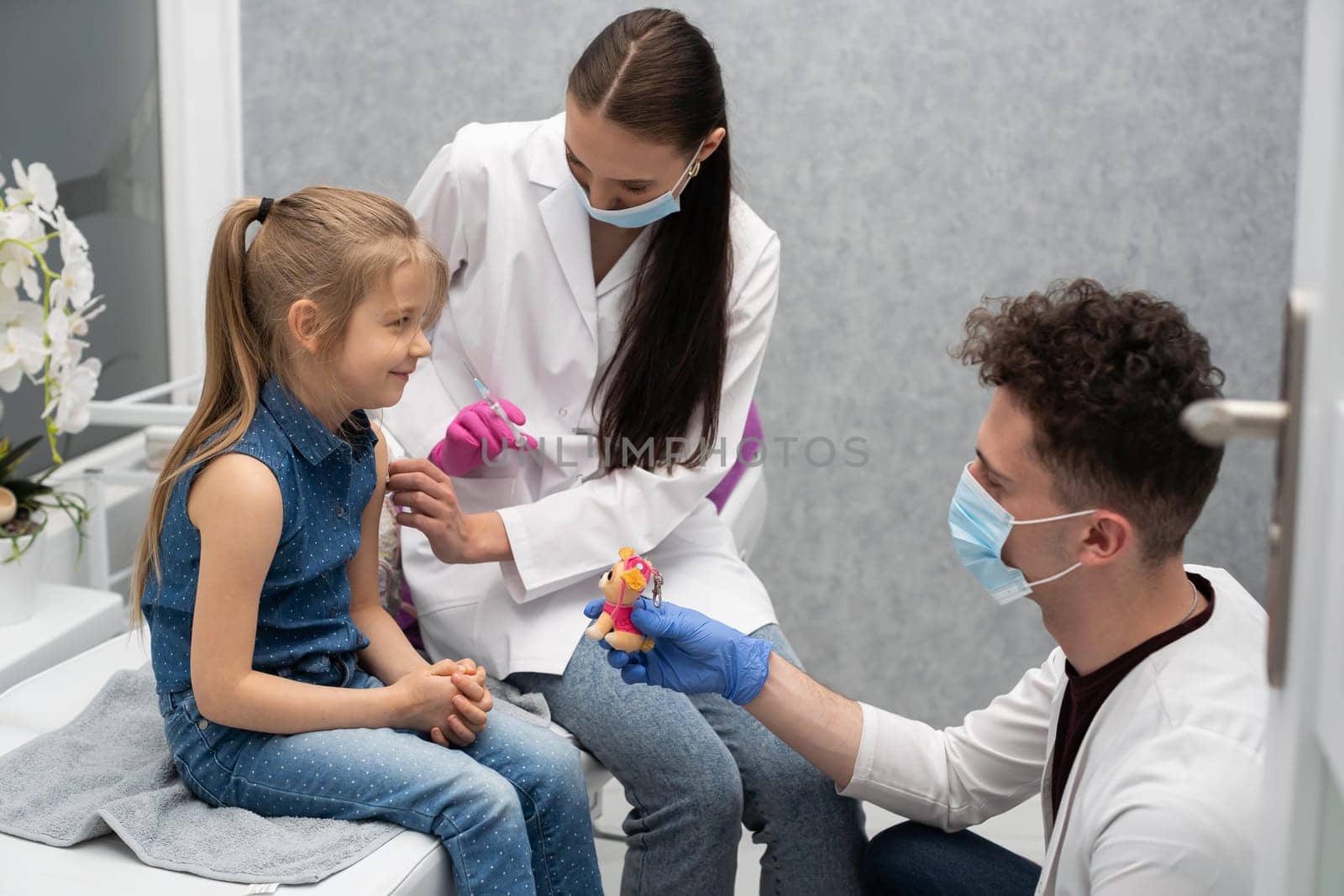 An apprentice in the last year of medicine talks to a little patient not to be afraid of injections. The doctor is getting ready to inject the new vaccine.