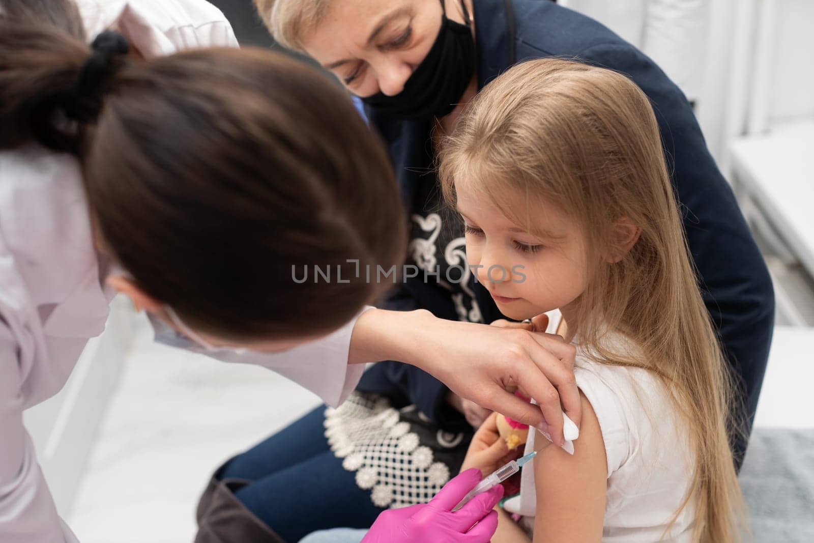 A grandmother with a good approach to young children encourages her granddaughter, who came to a doctor's office in a large hospital for the first time in her life. Safe vaccination of children.