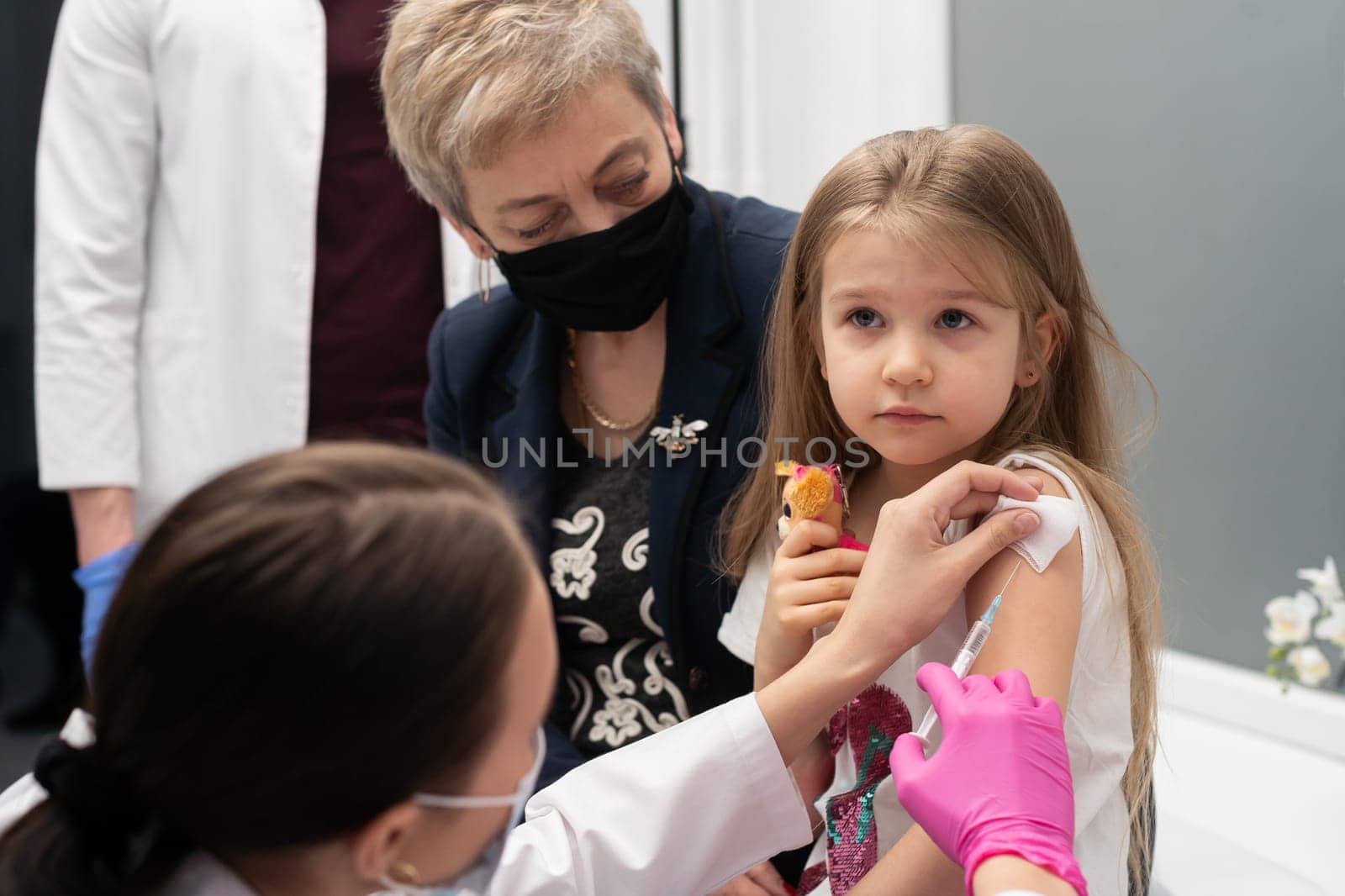 A grandmother with a good approach to young children encourages her granddaughter, who came to a doctor's office in a large hospital for the first time in her life. Safe vaccination of children.