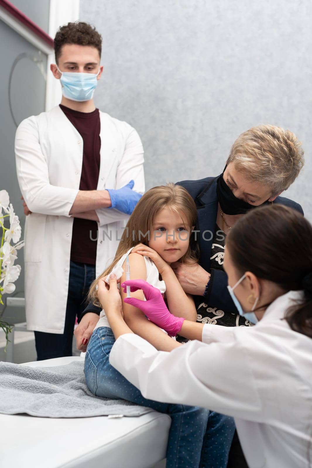 The girl came to the vaccination with her grandmother to feel safe in the doctor's office. A young nurse is injecting a new vaccine. Safe vaccination of children.