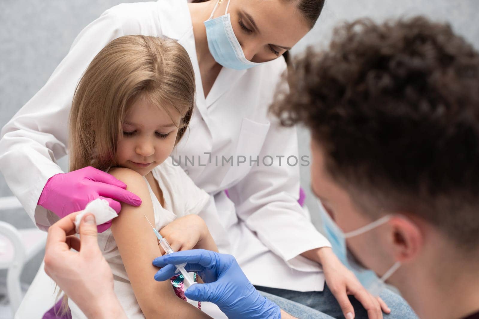 The nurse is sitting next to the girl about to be vaccinated by the doctor. A doctor's office in a public hospital. Safe vaccination of children.