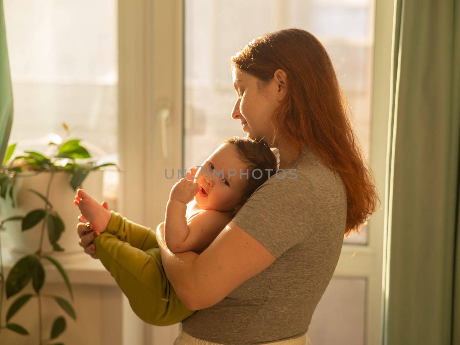 Caucasian woman tenderly holds her newborn son while standing near the window. by mrwed54