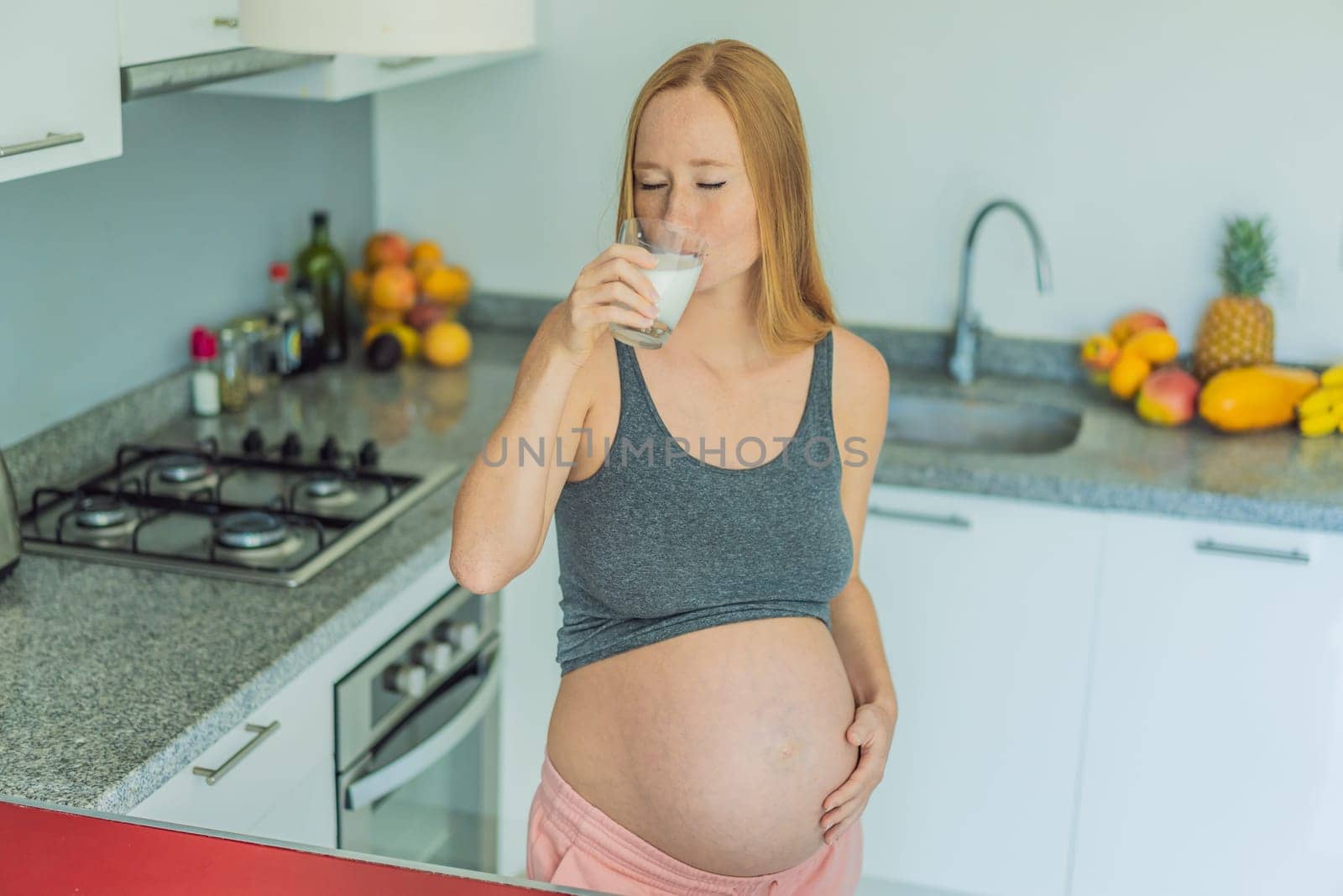 Weighing the pros and cons of milk during pregnancy, a thoughtful pregnant woman stands in the kitchen with a glass, contemplating the decision to include or avoid milk for her and her baby's well-being.