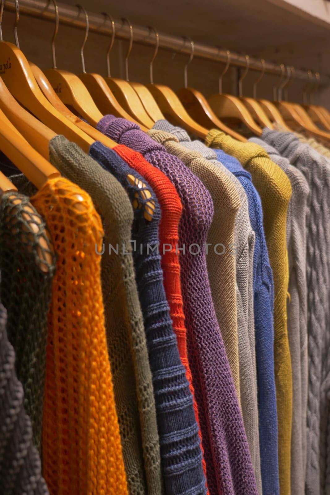 Colorful sweaters displayed on wooden clothes hangers.