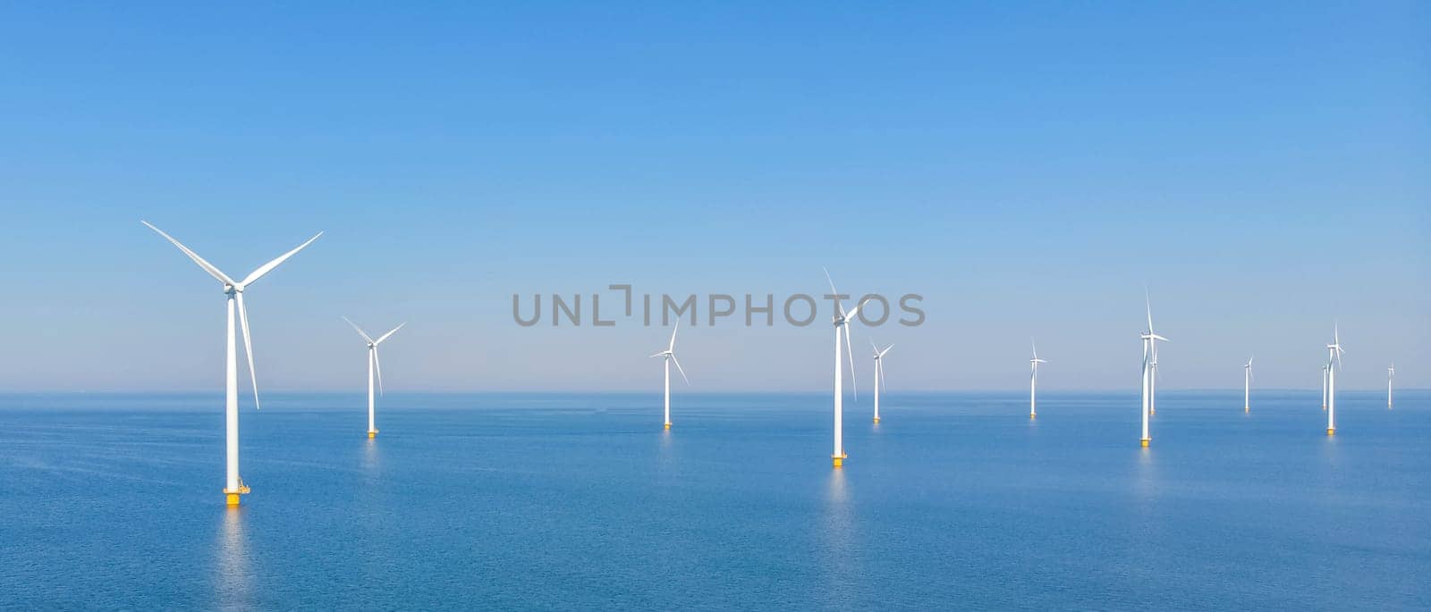 A wind farm with rows of wind turbines in the middle of the ocean, blending into the natural landscape between the water and the azure sky