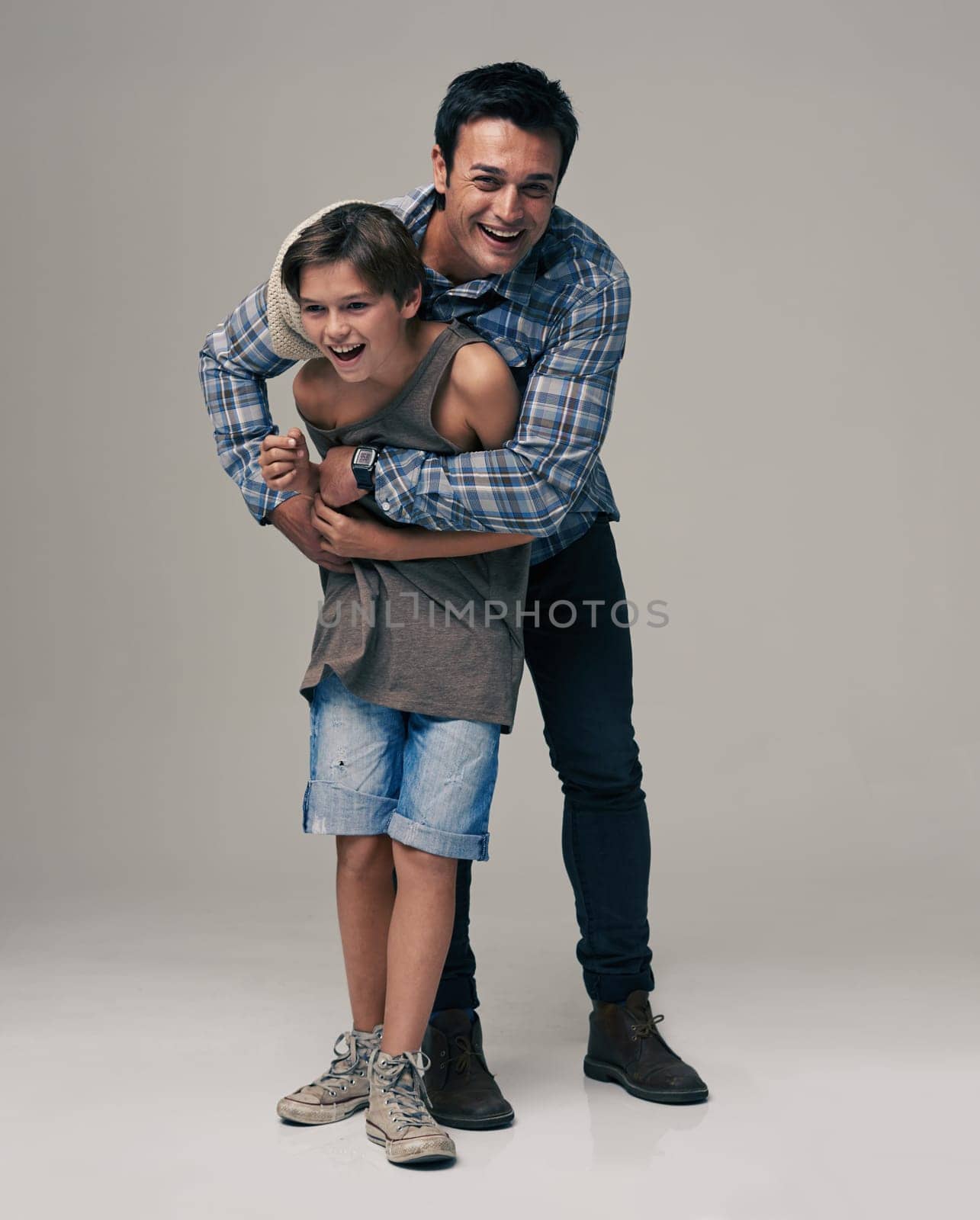 Happy father, portrait and child laughing with hug for love, care or support in fashion on a gray studio background. Dad playing with son or kid in happiness for parenting or bonding on mockup space.