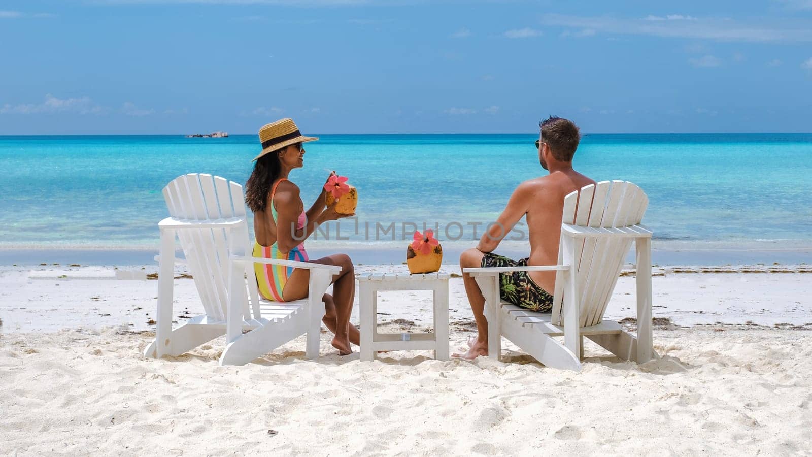 couple men and women on the beach with a coconut drink at Praslin Island Seychelles, couple on a luxury vacation relaxing at waterfront, man and woman on a tropical vacation