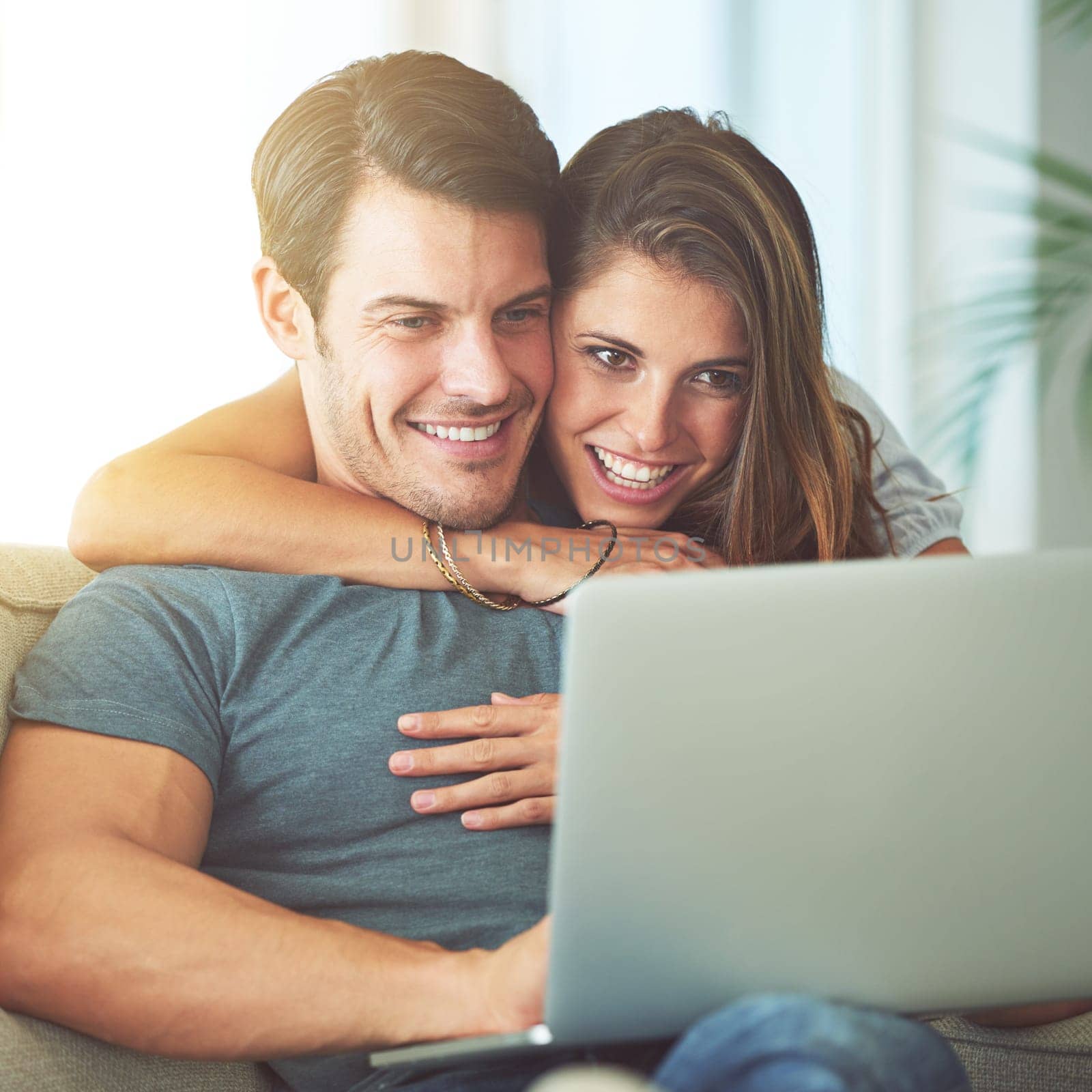 Laptop, happy and woman embracing man on sofa networking on social media, website or internet. Smile, love and female person hugging husband reading online blog with computer in living room at home