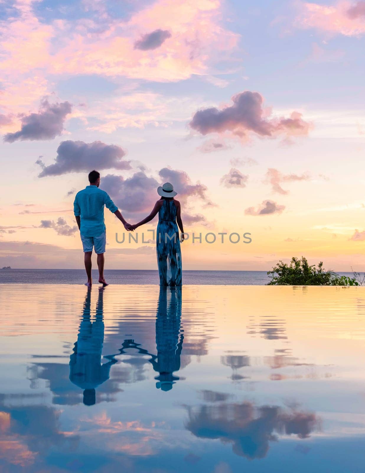 Young men and women watching sunset with reflection in the infinity pool at Saint Lucia Caribean by fokkebok