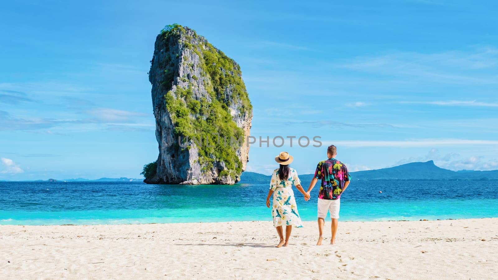 Diverse couple of Asian women and European men walking on the tropical beach of Koh Poda Island Krabi Thailand. Beautiful tropical beach in Thailand with a limestone cliff island in front, rear view