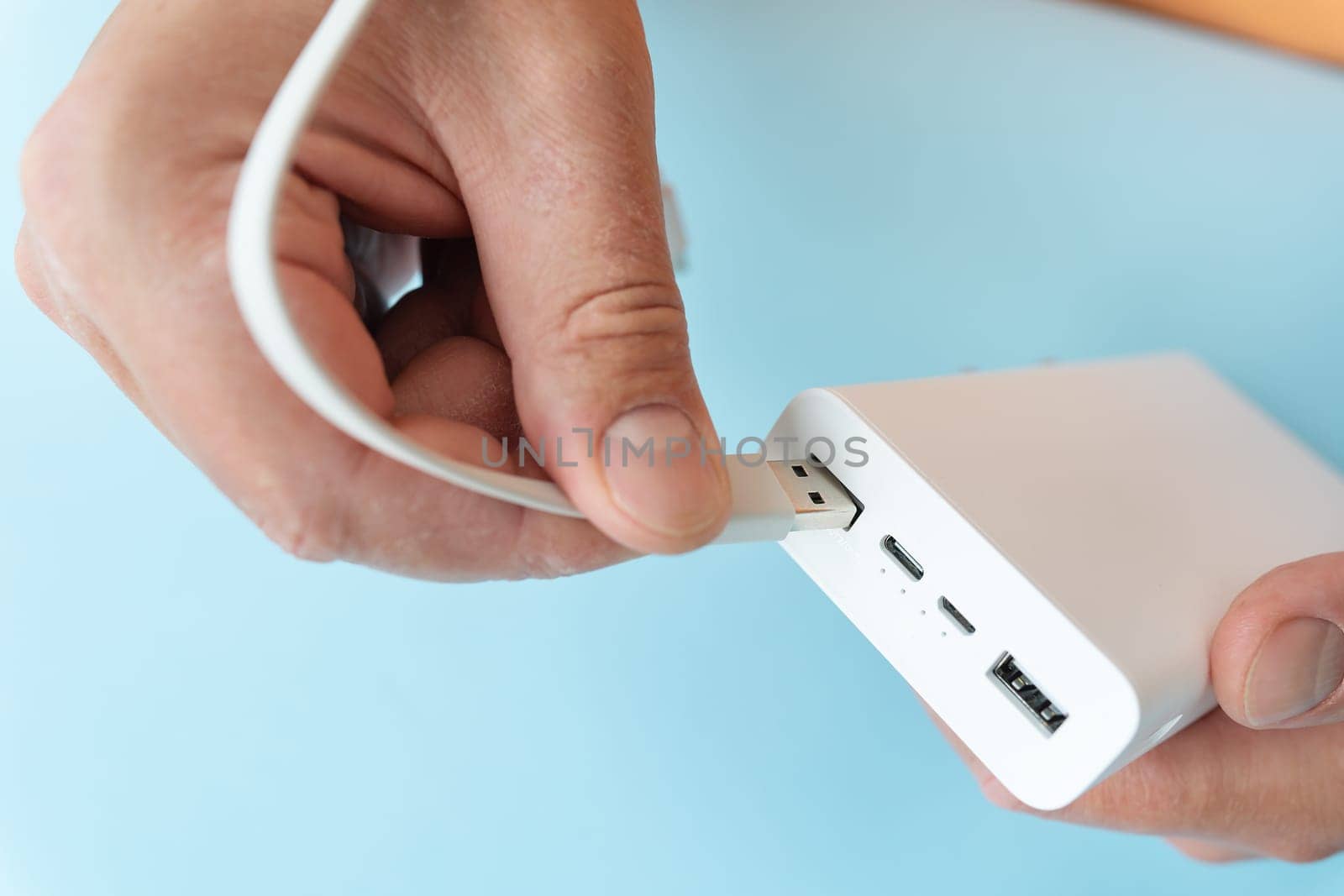 Close-up of a hand connecting a USB cable to a white power bank on a blue background