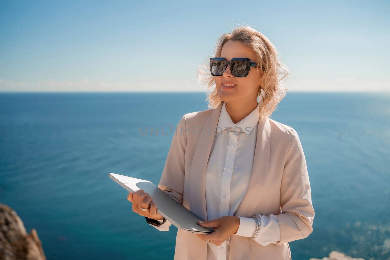 Freelance women sea working on a computer. Pretty middle aged woman with computer and phone outdoors with beautiful sea view. The concept of remote work