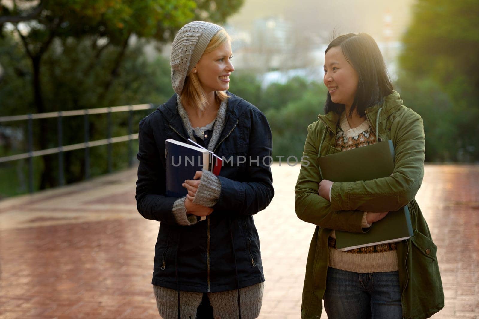 Students, women and friends on campus for university, conversation while walking to class and smile outdoor. College, communication and books for studying, education and academic growth with talk.