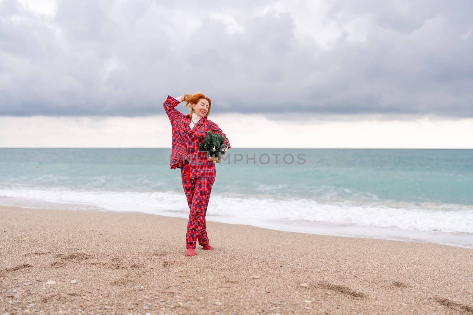 Sea Lady in plaid shirt with a christmas tree in her hands enjoys beach. Coastal area. Christmas, New Year holidays concep by Matiunina