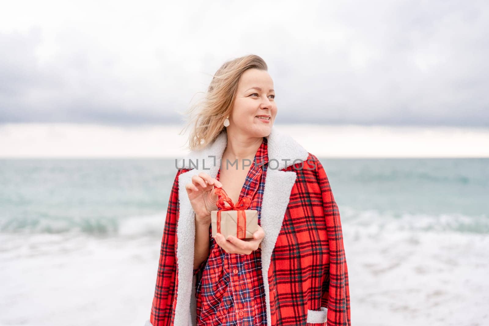 Lady in plaid shirt holding a gift in his hands enjoys beach. Coastal area. Christmas, New Year holidays concep.