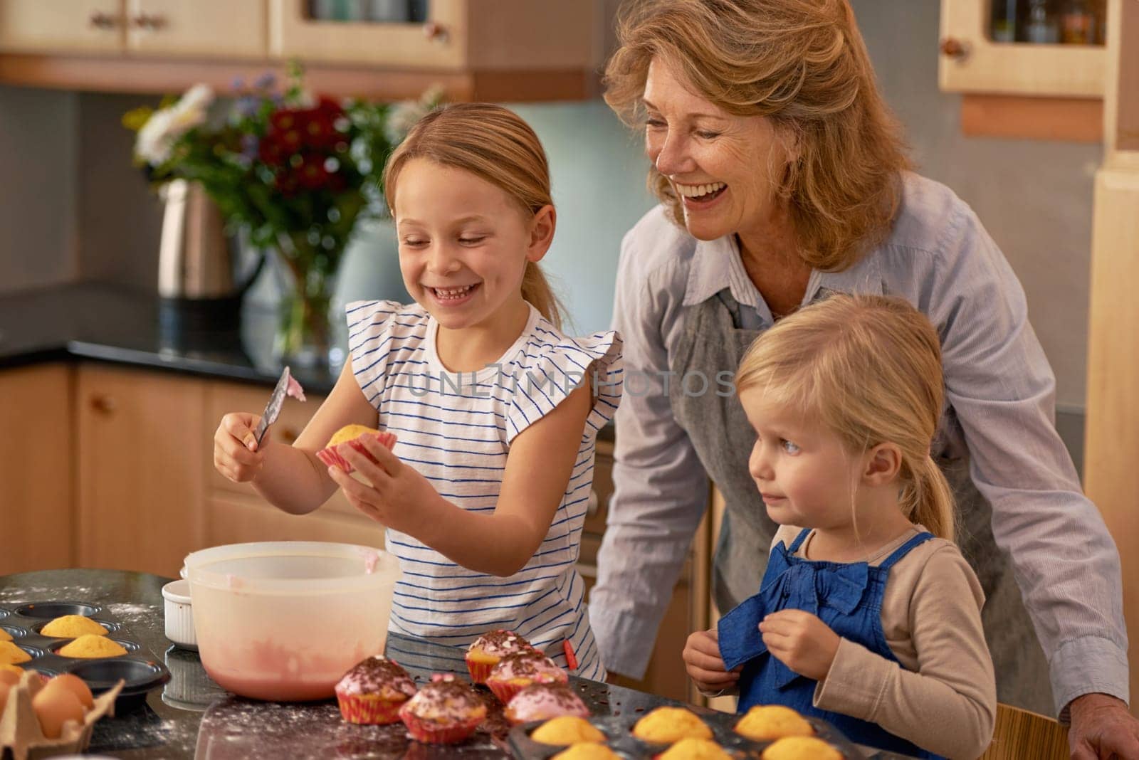 Mature woman, children and smile for baking in retirement for family, fun and bonding at home. Happy, female pensioner and girl with cupcake, laugh and icing for creative fun together in kitchen.