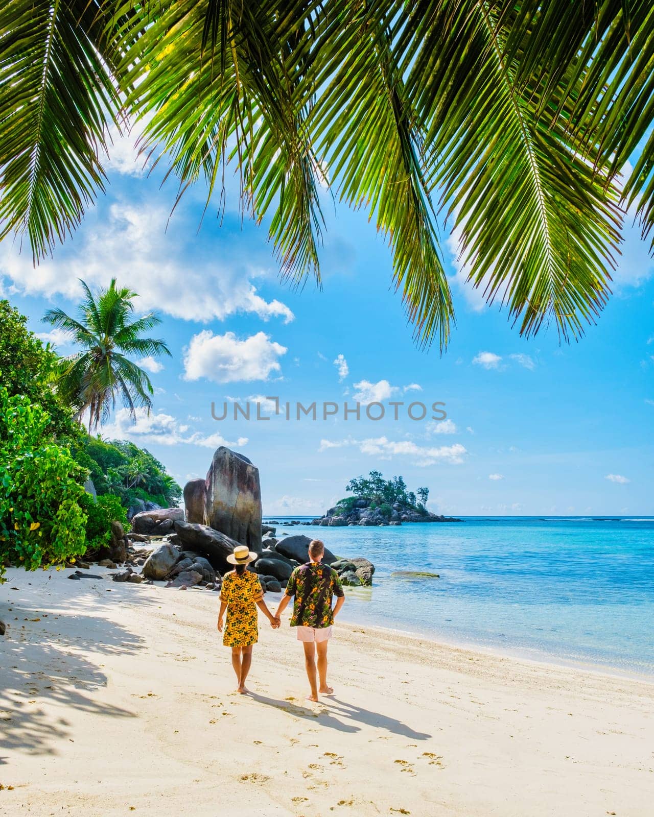 man and woman on vacation in Seychelles Mahe, a tropical beach with palm trees and a blue ocean Anse Royale Beach, a diverse couple of Asian women and caucasian men walking hand together on the beach