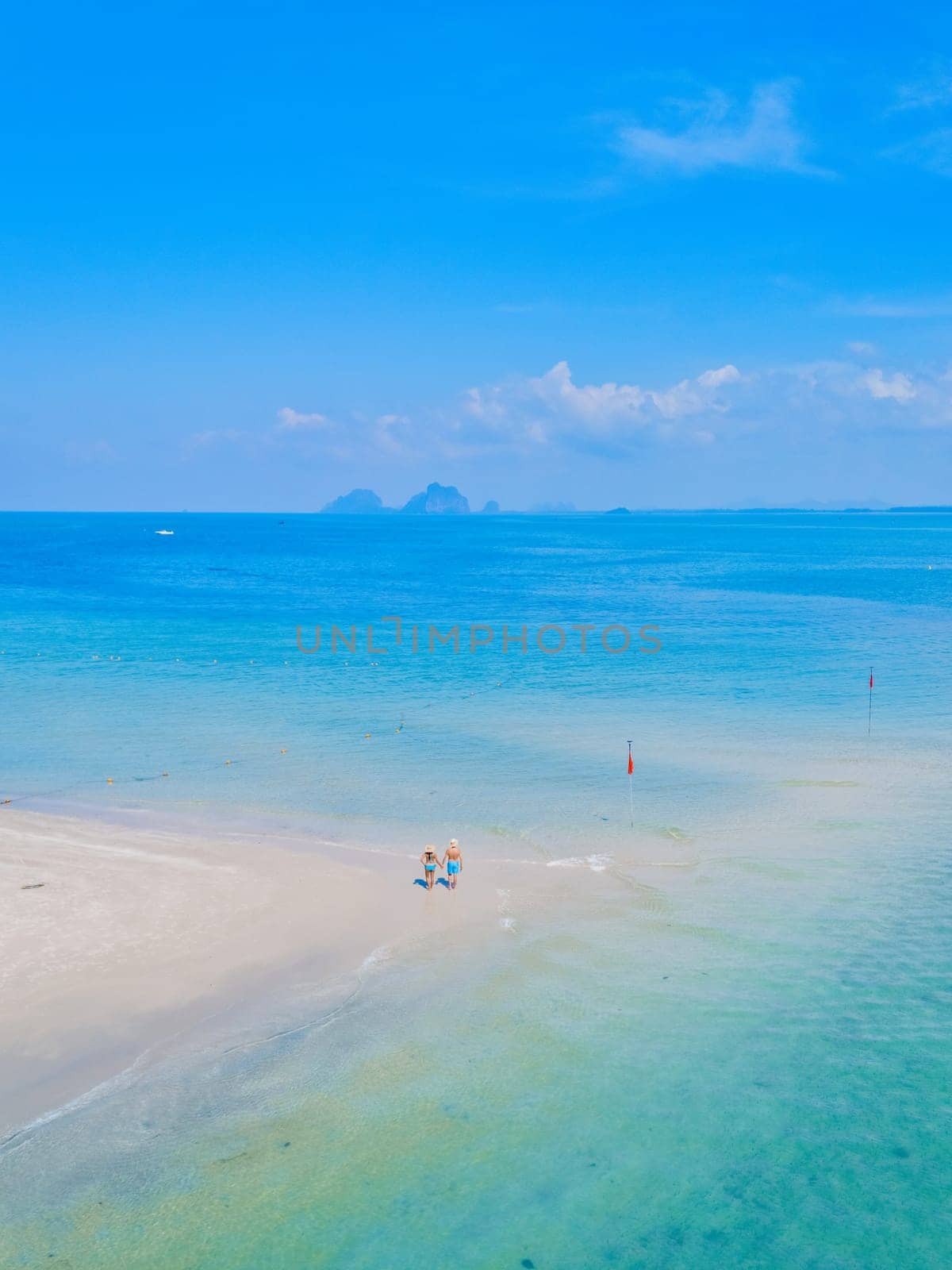 a couple of men and woman walking at the beach during a tropical vacation in Thailand, Koh Muk a tropical sandbar in a blue ocean with soft white sand, and a turqouse colored ocean Koh Mook Thailand