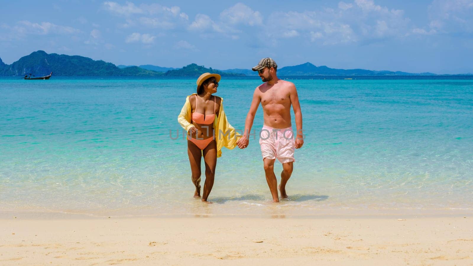 a diverse couple of men and women walking from the ocean to the beach of Koh Kradan Island Thailand, caucasian men, and Asian women summer vacation, traveling around Thailand