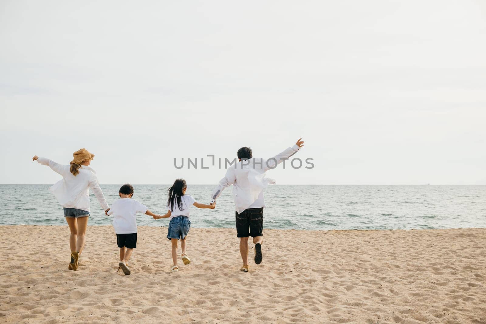 A heartening family scene on the beach parents holding hands running and jumping with their children in holiday laughter. Illustrating the happiness and togetherness of a carefree beach vacation.