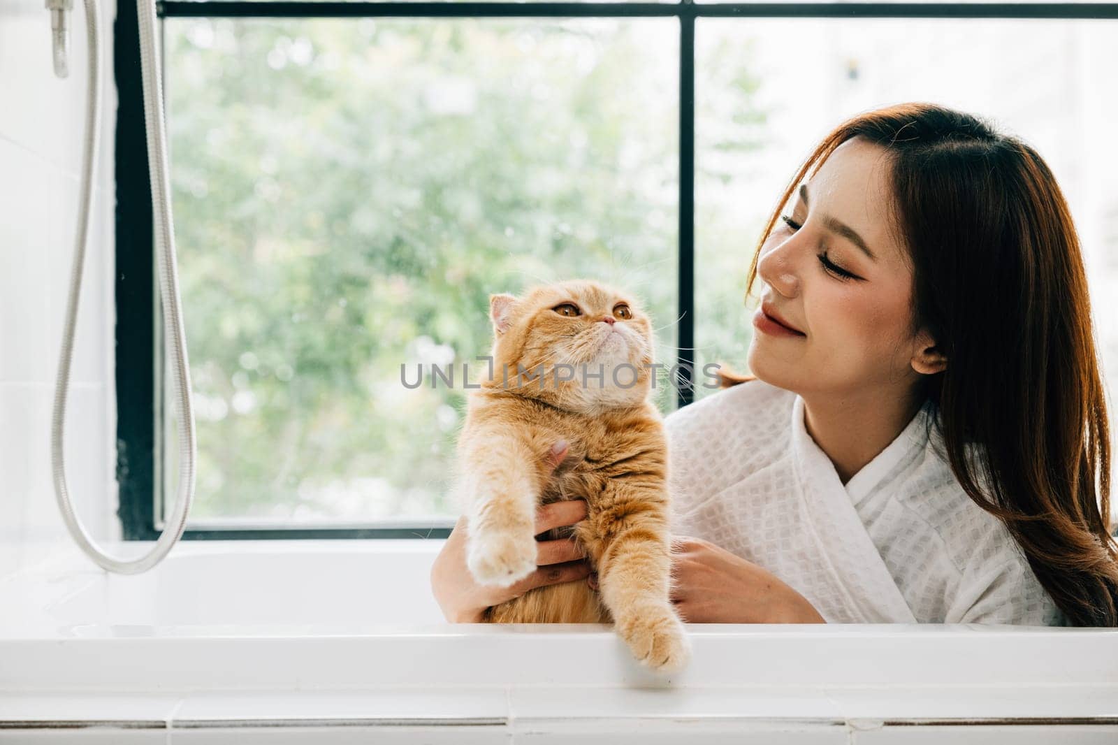 Bath time bonding, a woman holds her Scottish Fold cat in the bathtub, radiating happiness and the warmth of pet companionship in the bathroom.