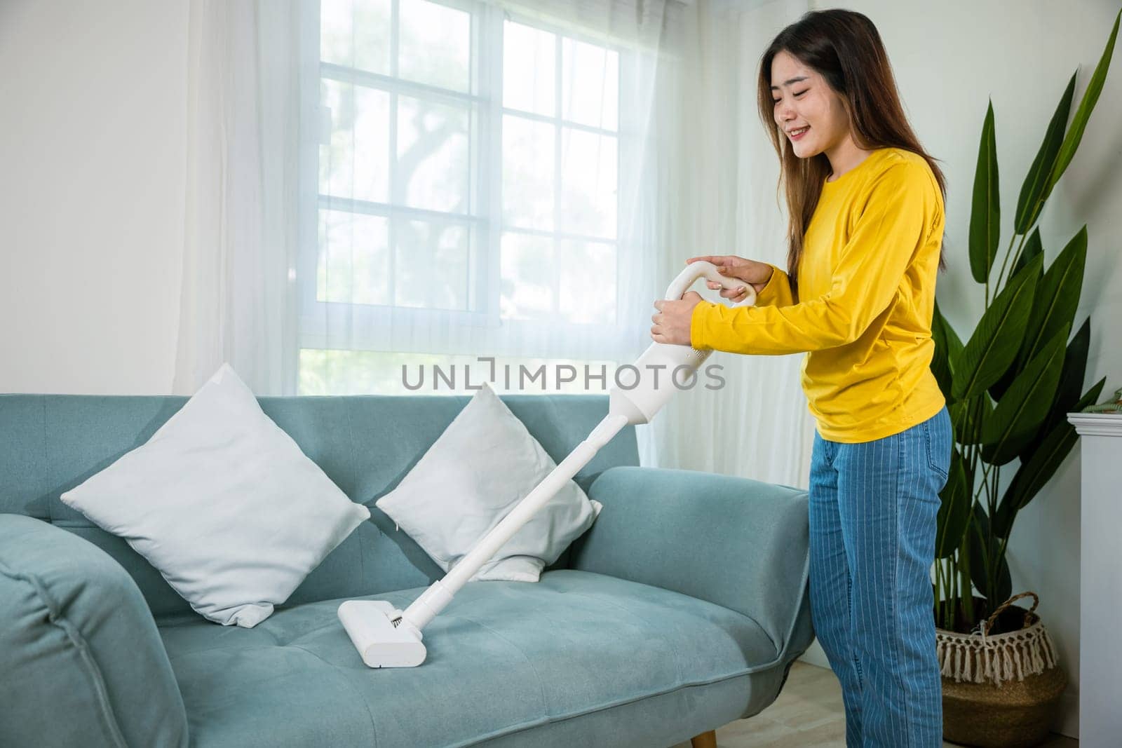 Happy Asian young woman with accumulator vacuum cleaner at home in living room by Sorapop