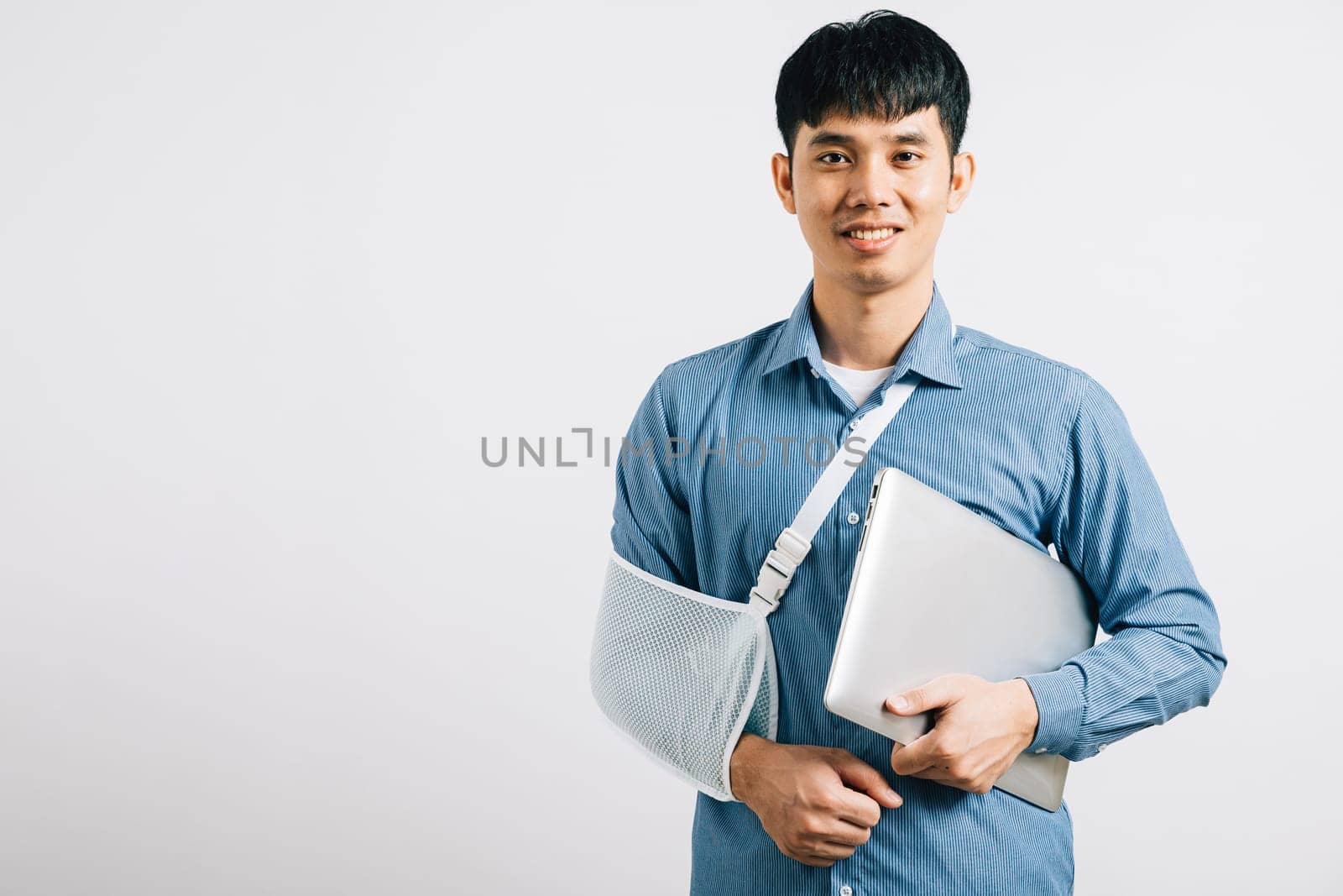A resilient business professional, with a broken arm, utilizes a splint while working on a laptop. Studio shot isolated on white, highlighting determination and recovery. Copy space available.