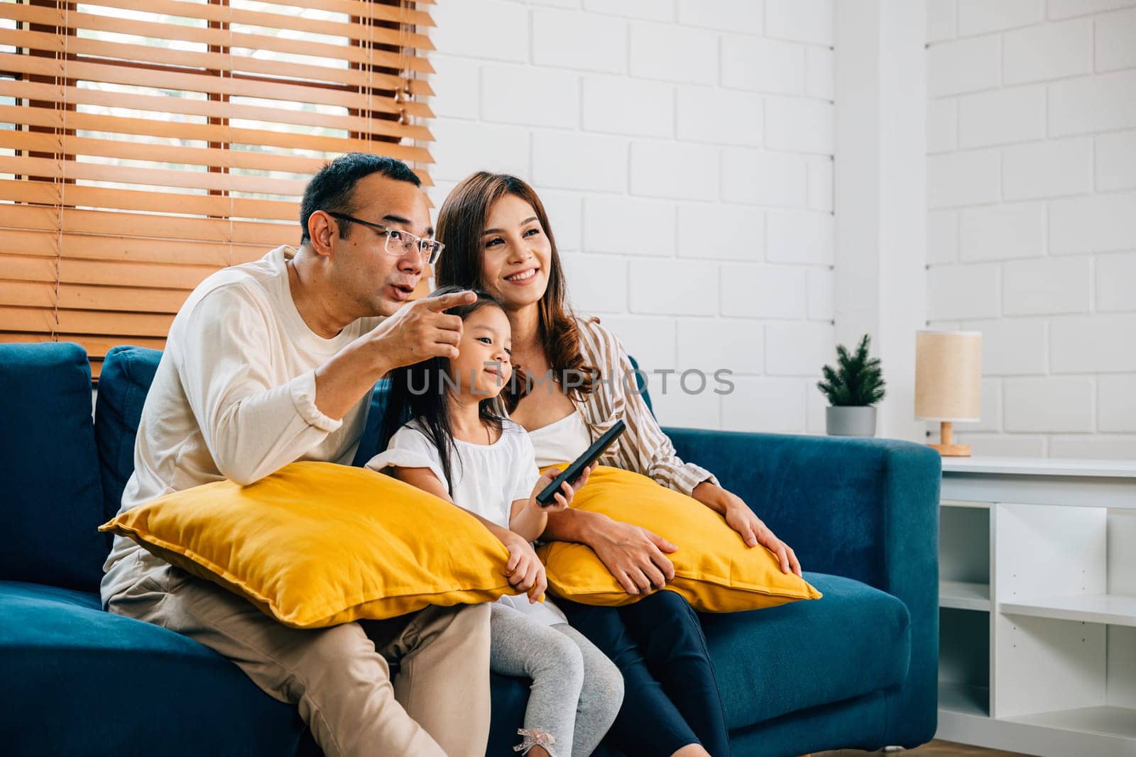 A cheerful Asian family finds relaxation and togetherness watching TV at home. The father mother son and daughter share precious moments of laughter and fun during their weekend time.