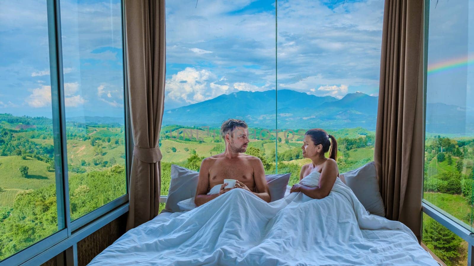 a couple of men and woman laying in bed with open widows looking out over the mountains of Thailand by fokkebok