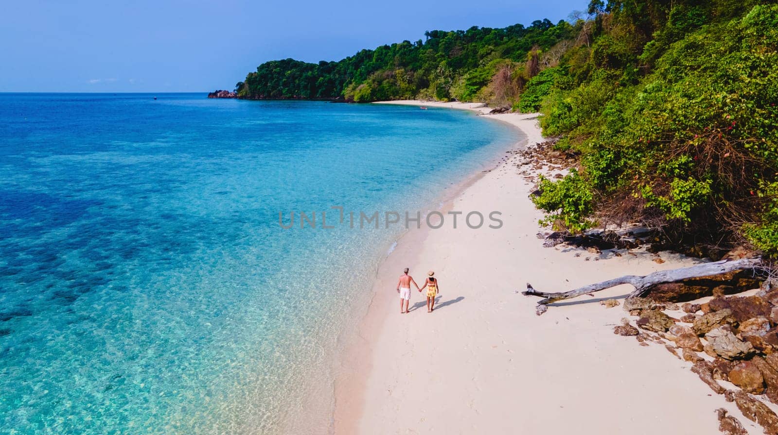 top view at a couple walking on a tropical beach, white soft sandy tropical beach and turqouse colored ocean. men and women on the beach seen from above with a drone