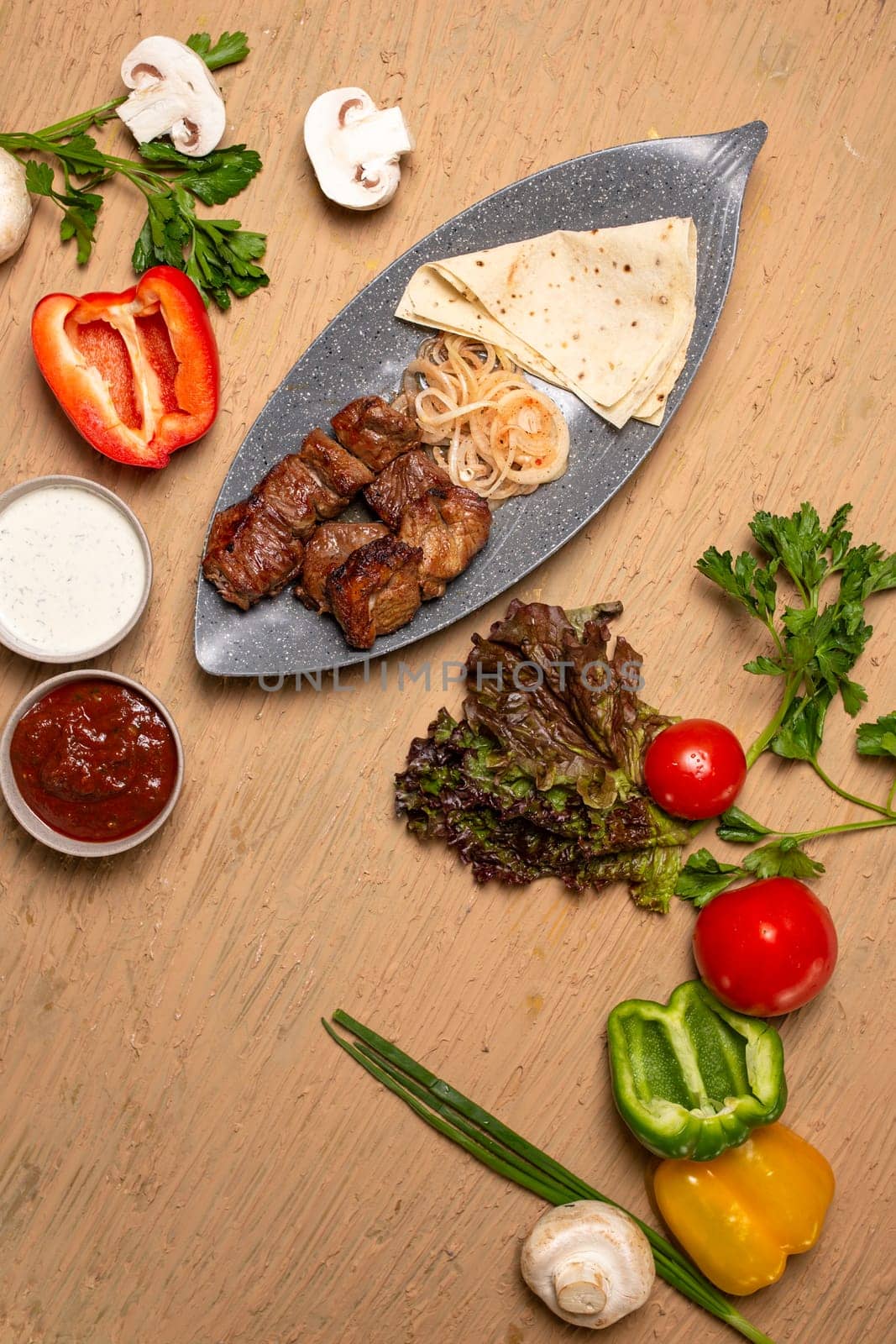 Grilled meat and vegetables on a rustic wooden table with soft flatbread. Succulent meat, tender veggies, vibrant tomatoes, peppers, mushrooms, onions create a delicious meal.