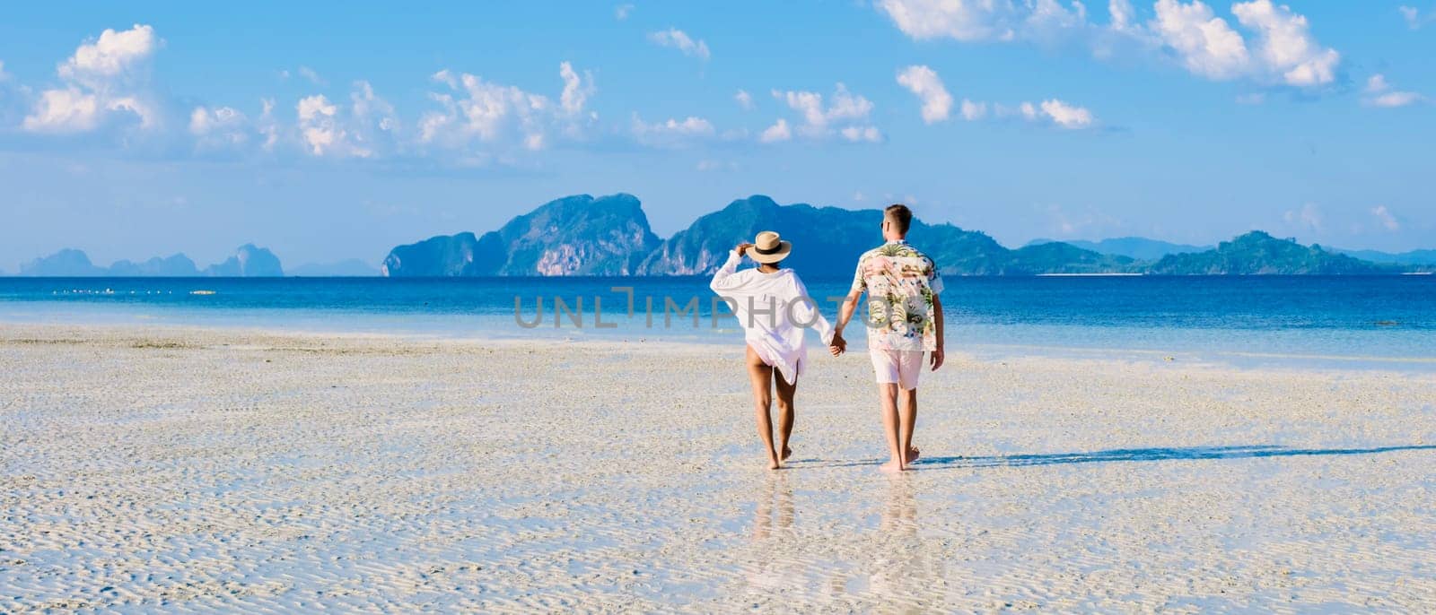 rear view of a couple of men and women walking at the beach at sunset, Koh Kradan island in Thailand during vacation on a sunny day, holiday in Thailand, summer trip, weekend getaway