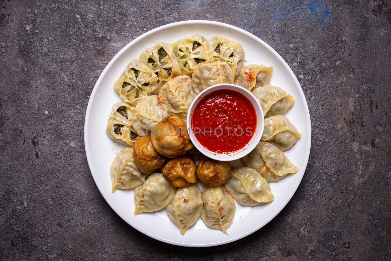 Uzbek samsas and manti with meat, pumpkin and greens on a plate with red sauce by Pukhovskiy