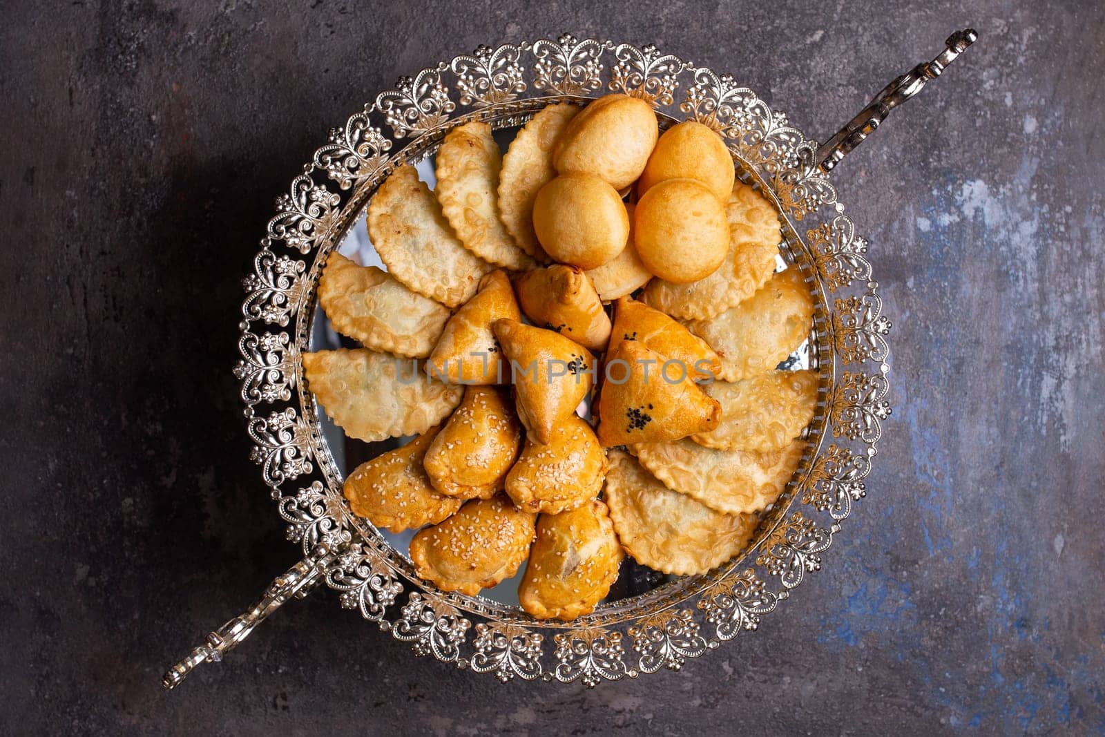 An assortment of delicious pastries, including baklava, borek, and bourekas, is artfully arranged on a silver platter.