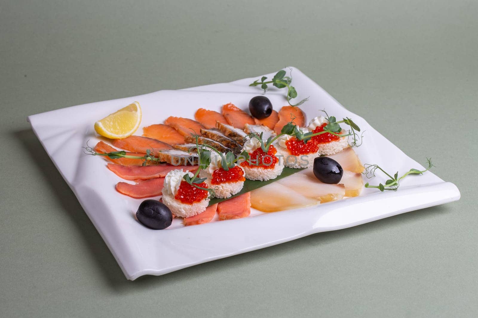 An artfully arranged platter of fresh seafood - salmon, trout, caviar, and shrimp - on a white plate with lemon slices and greens. A visually appealing still life composition.