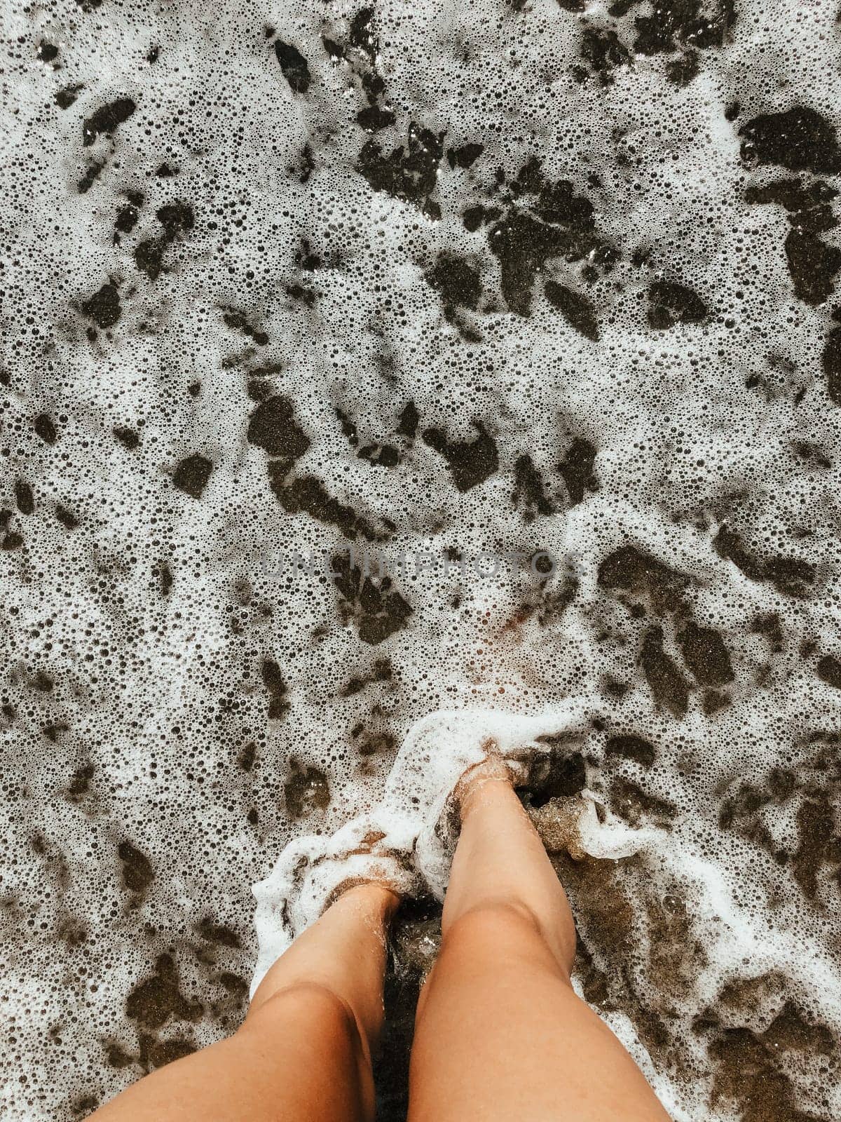 Woman legs barefoot at sea foam waves on sand beach summer day. top view above women feet. Ocean clear water seafoam. girl on beach Summer background nature concept holiday vacation. natural wallpaper
