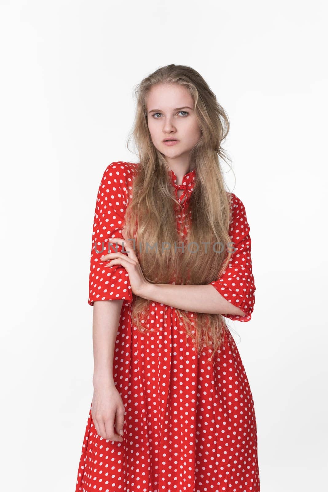 Fashionable blonde woman with long hair dressed in summer polka dot dress poses on white background by Alexander-Piragis