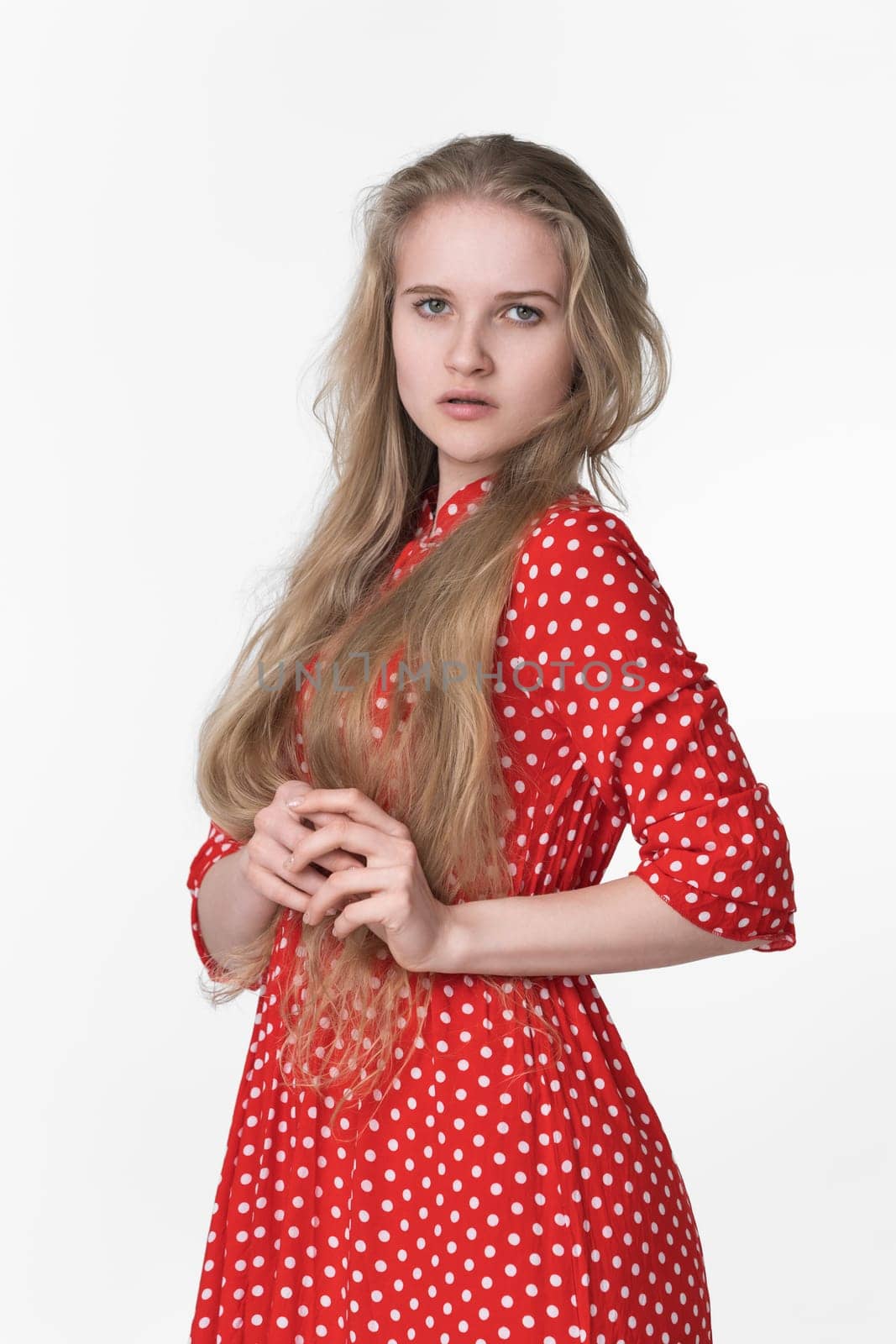 Elegant young blonde female with long hair dressed in summer red polka dot dress on white background by Alexander-Piragis