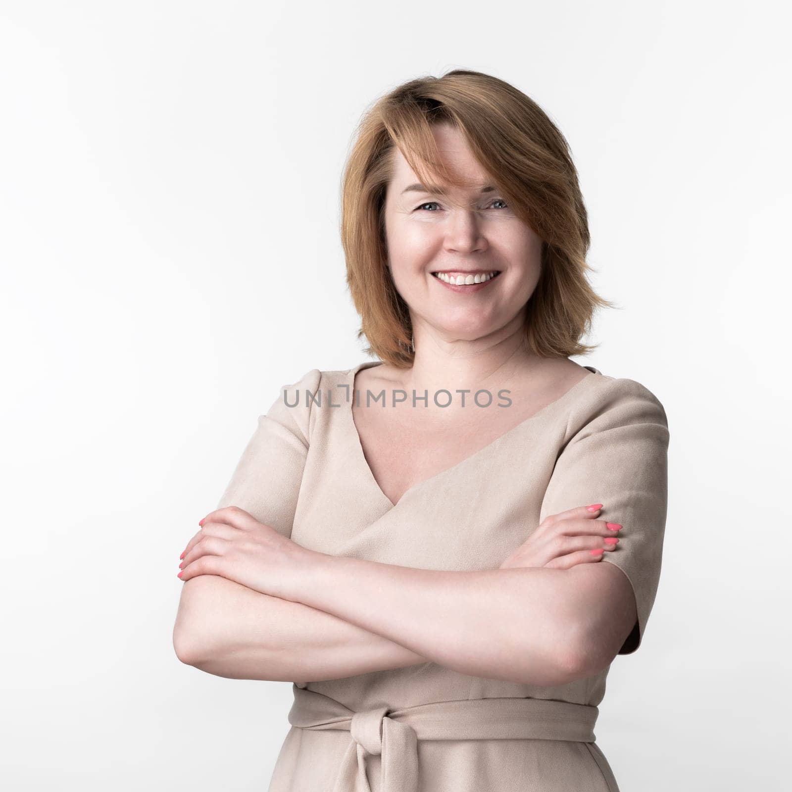 Mature Caucasian woman in casual dress looking at camera, crossing arms over chest. White background by Alexander-Piragis