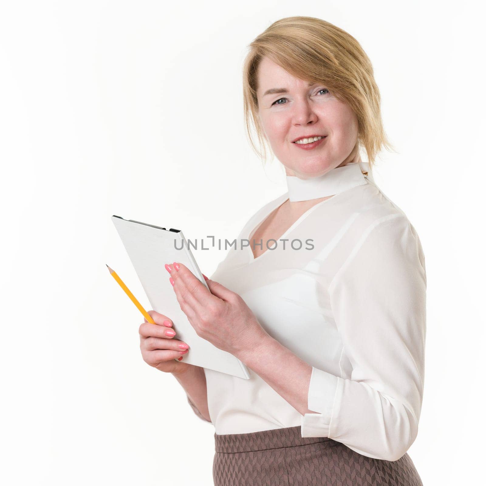 Portrait of sincere smiling and happy 49-year-old blonde businesswoman holding clipboard and pencil in hands, wearing in white blouse. Friendly and experienced woman entrepreneur looking at camera