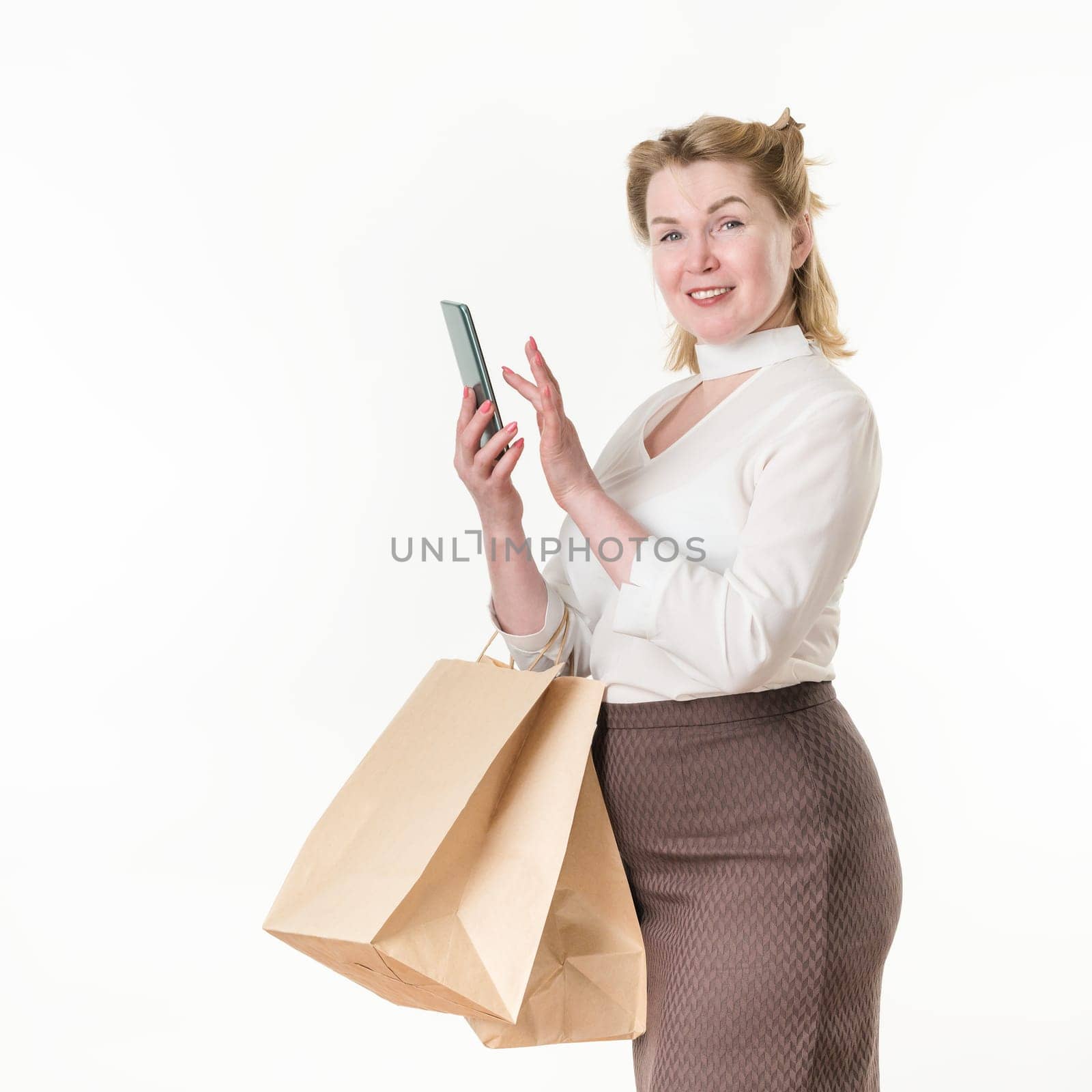 Woman buyer holds smartphone in hand and orders in an online shopping store. Satisfied caucasian ethnicity female 49 years old dressed in white blouse and brown skirt. Studio shot on white background