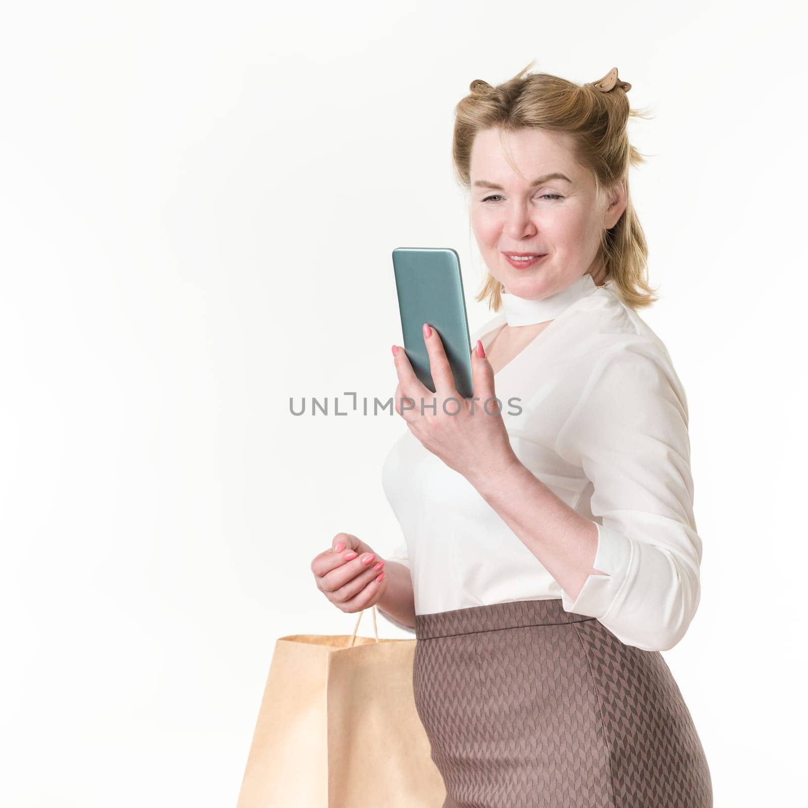 Happy shopaholic women using mobile phone for making payment. Black Friday and shopping online concept. 49 years old smiling woman shopper in white blouse and brown skirt on white background