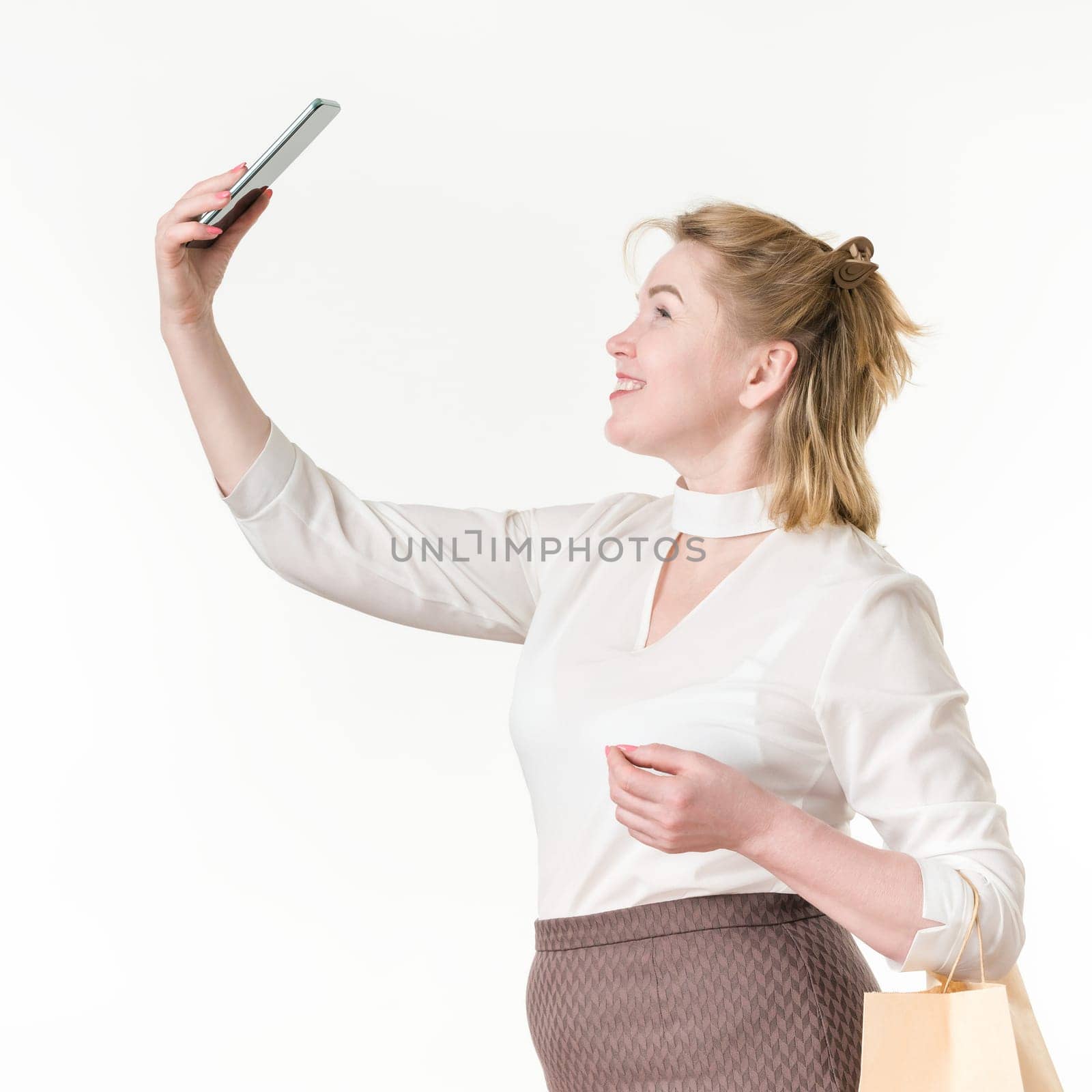 Caucasian ethnicity woman taking selfie holding phone up high, holding shopping bags with purchases by Alexander-Piragis