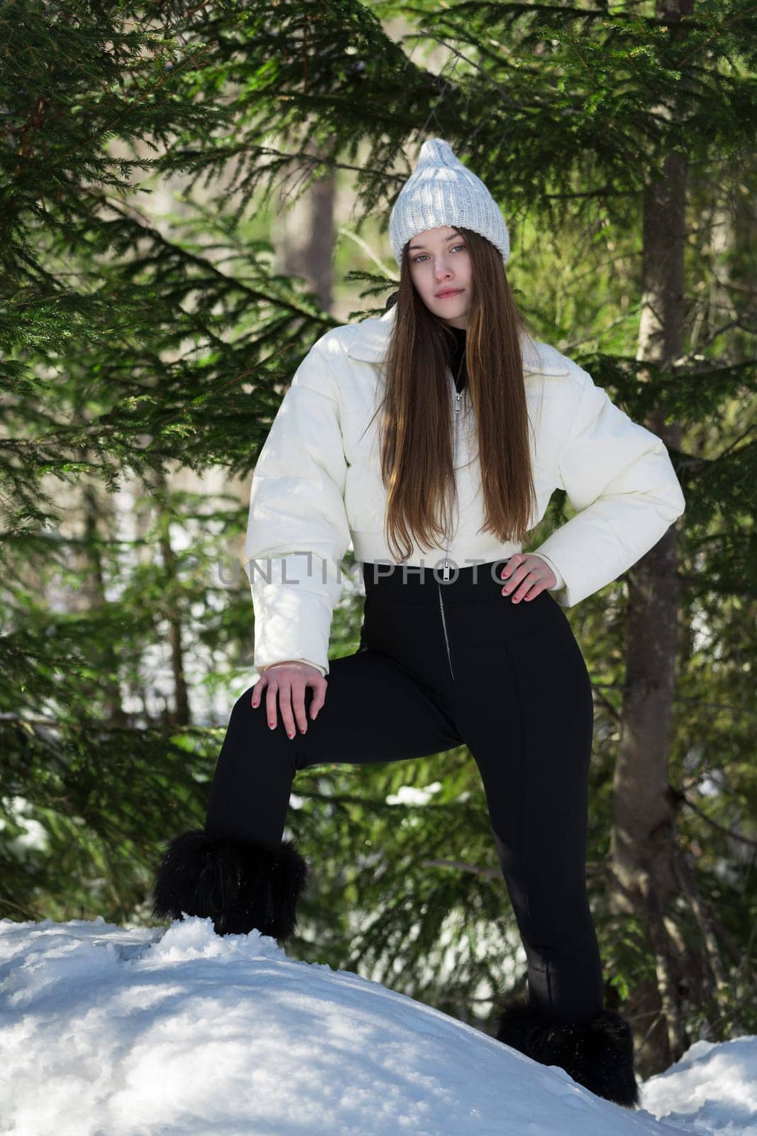 Teenager girl standing in winter forest in snowdrift on background of pine trees, looking at camera by Alexander-Piragis