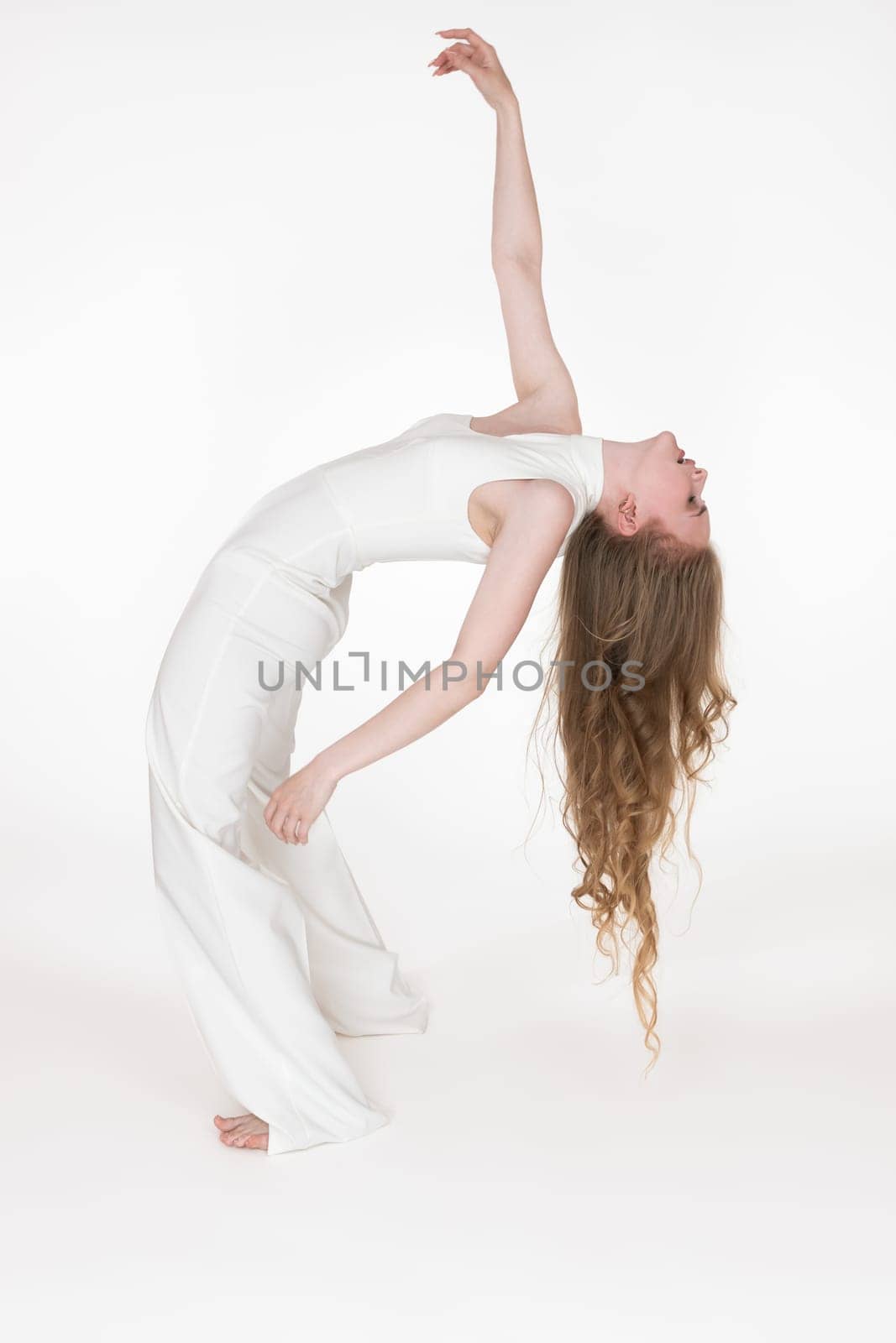 Full length view of flexible young woman dancer bending over backwards with eyes closed. Side view by Alexander-Piragis