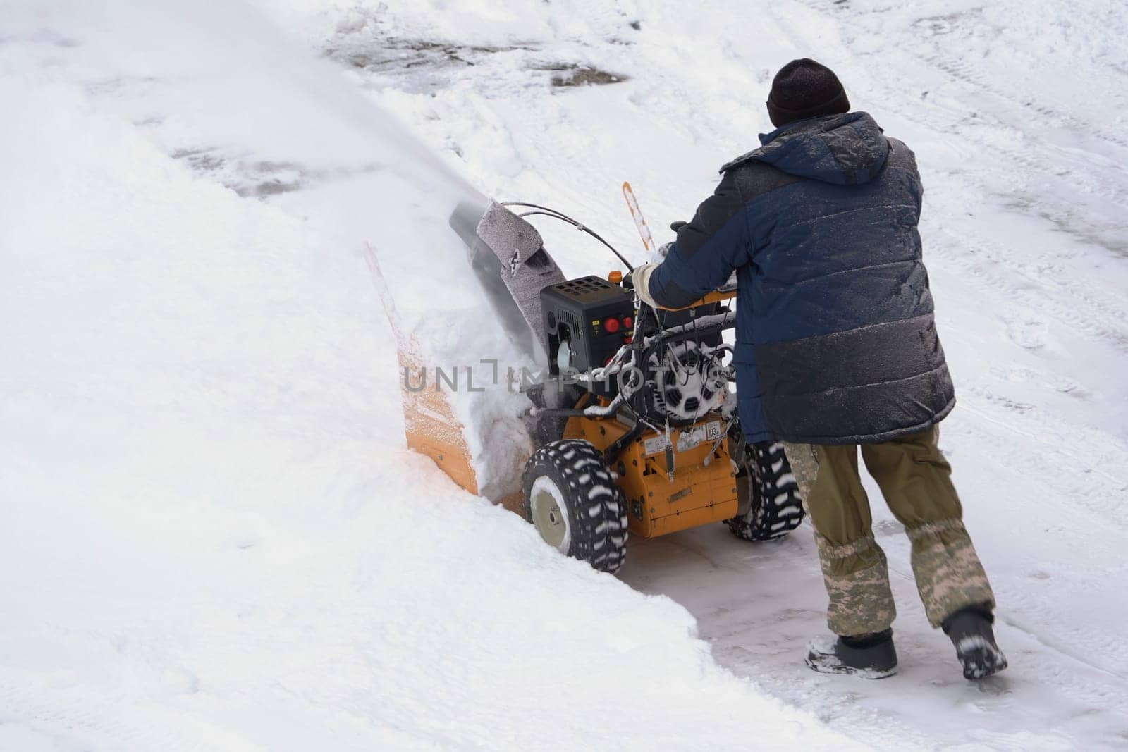 KAMCHATKA, RUSSIA - DEC 28, 2023: Man using snow blower to remove snow after winter storm. He is assisted by a snow thrower on a winter road. Man with snow blower on winter road after blizzard