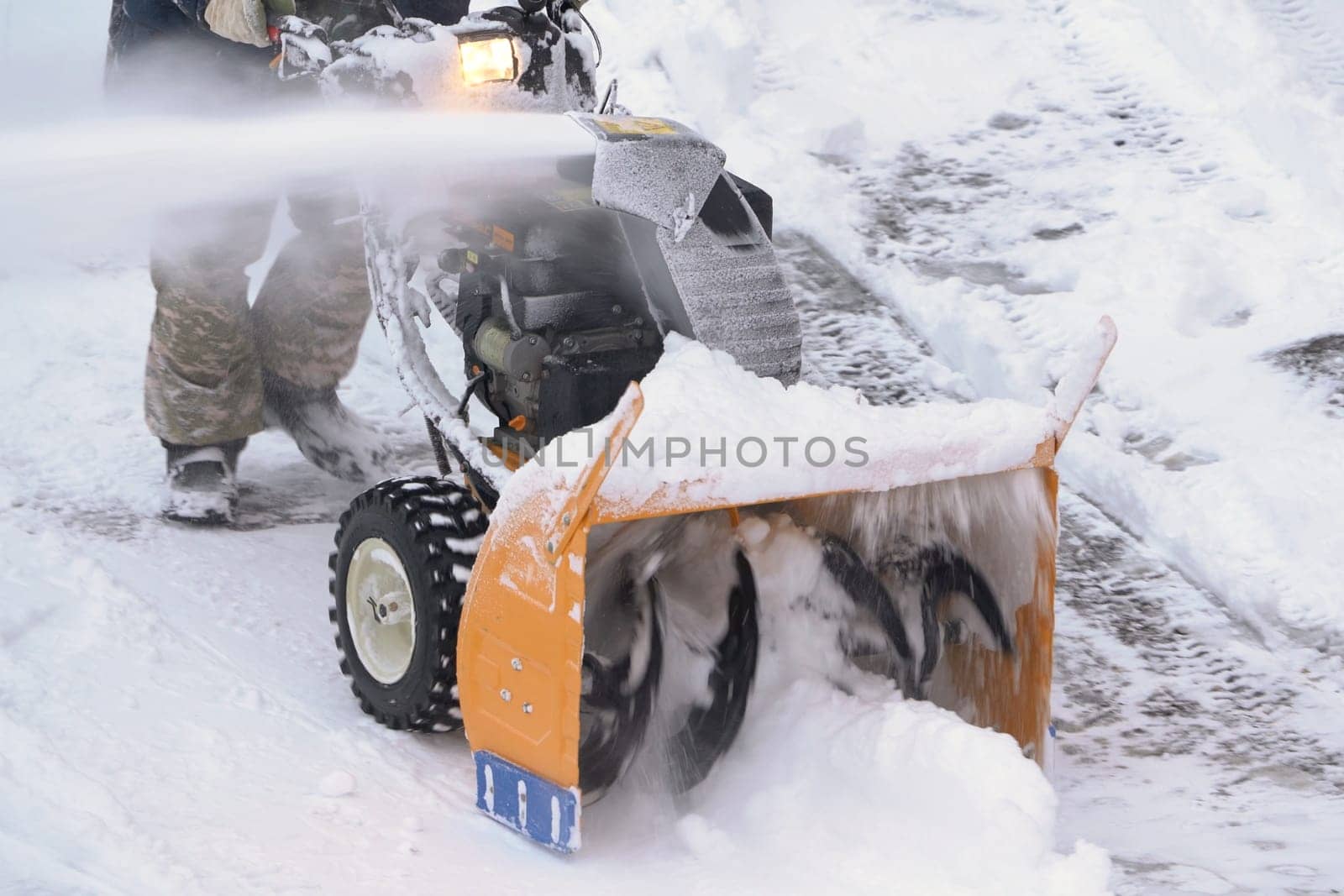 KAMCHATKA PENINSULA, RUSSIA - DEC 28, 2023: A male worker is using a snowblower machine to clear snow from the road after a winter storm. The worker is blowing snow following a blizzard