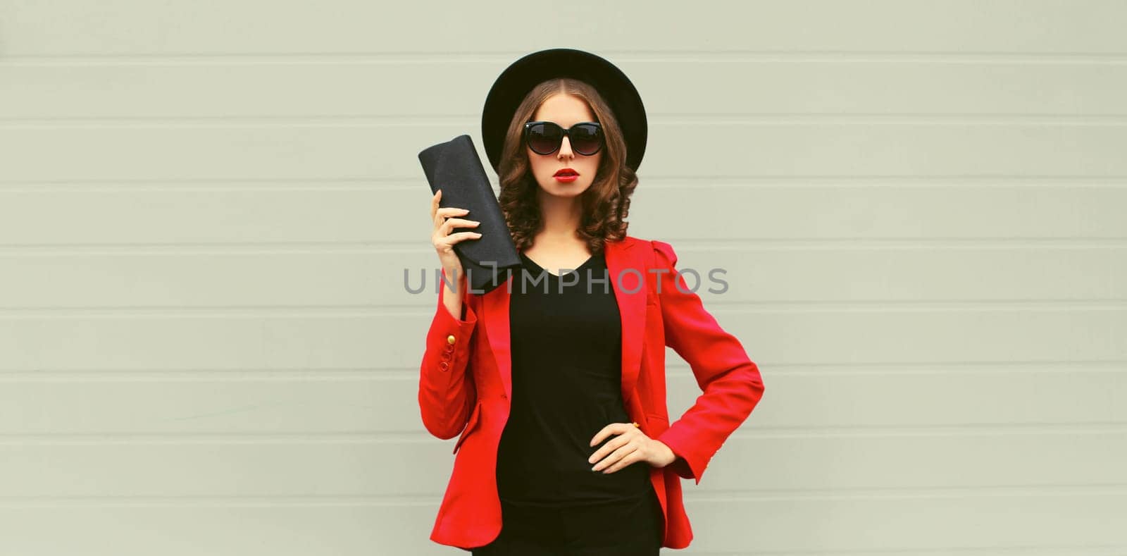 Stylish elegant woman posing in business suit, red blazer jacket, black round hat with handbag clutch
