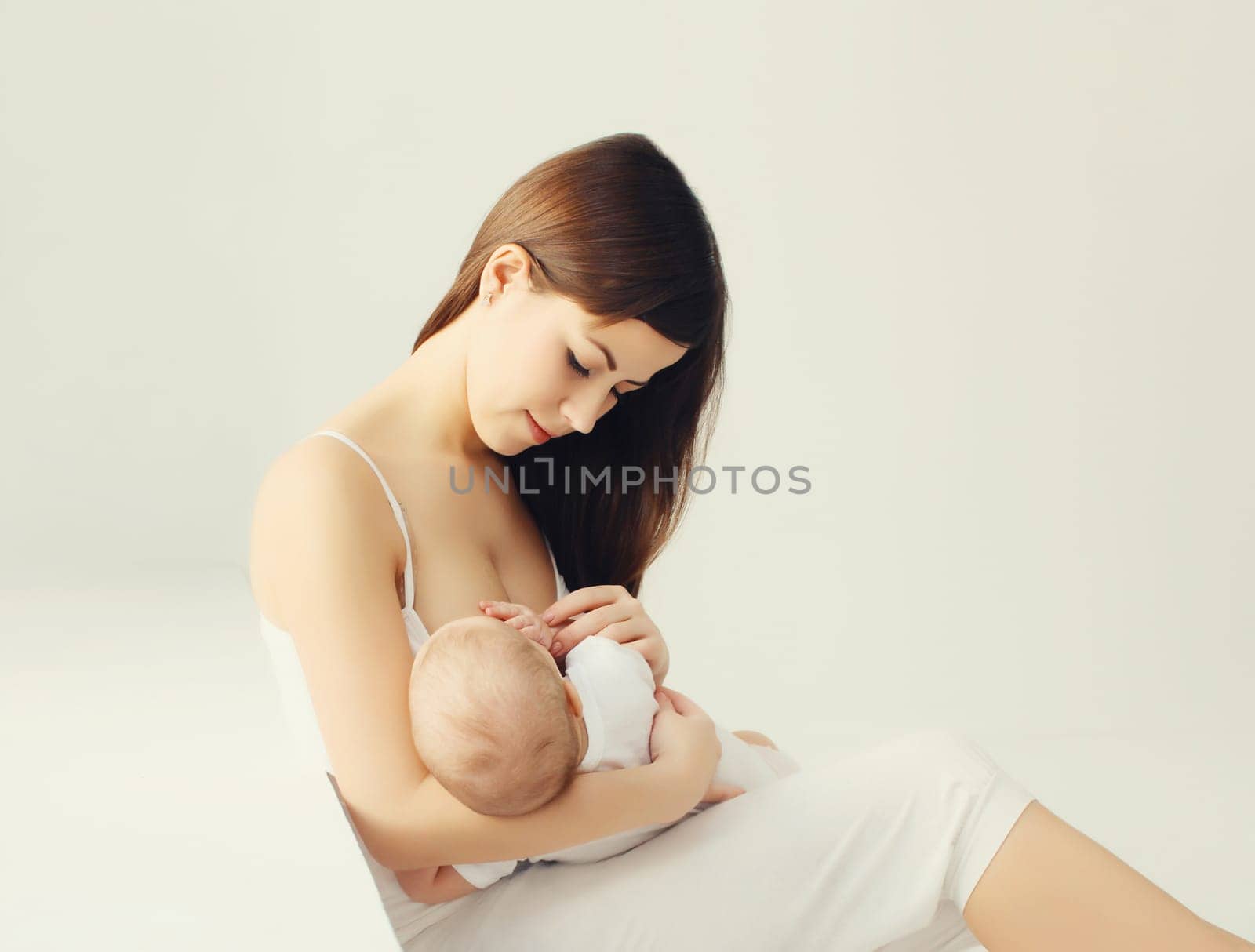 Portrait of happy young mother breastfeeding her baby at home on white background