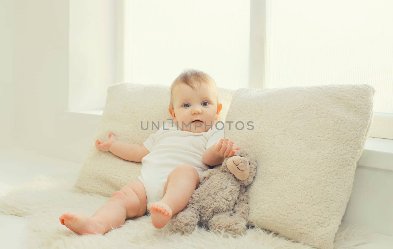 Happy cute little baby playing with teddy bear toy on the floor in white room at home
